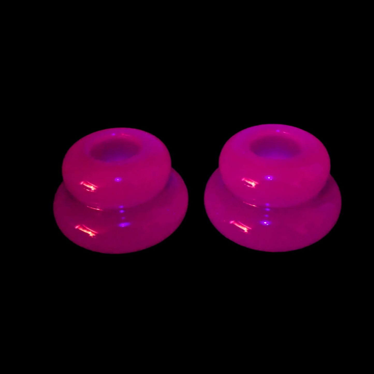 Photo of the neon purple handmade resin puffy round double ring candlestick holders fluorescing pink under a UV light.