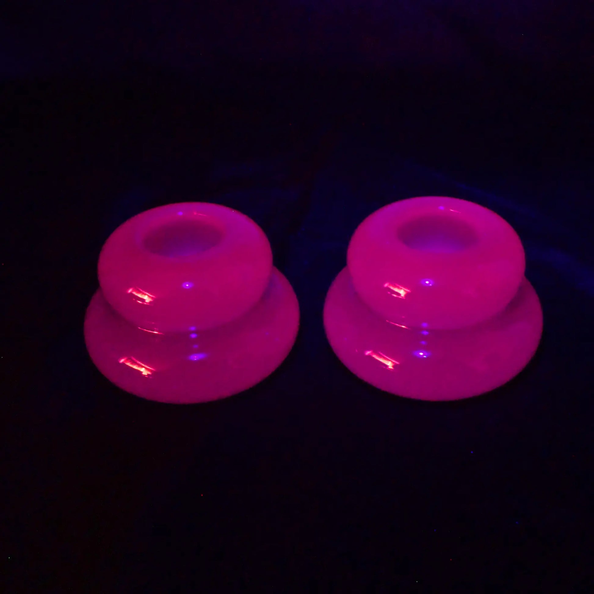 Photo of the neon purple handmade resin puffy round double ring candlestick holders fluorescing pink under a UV light.
