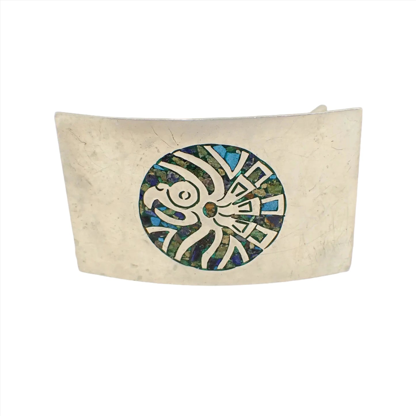 Front view of the vintage Alpaca Mexican belt buckle. It has a Southwestern Mayan design of Cuauhtli eagle bird with inlaid stone chips in different colors. The metal is silver tone in color and is rectangle shaped.