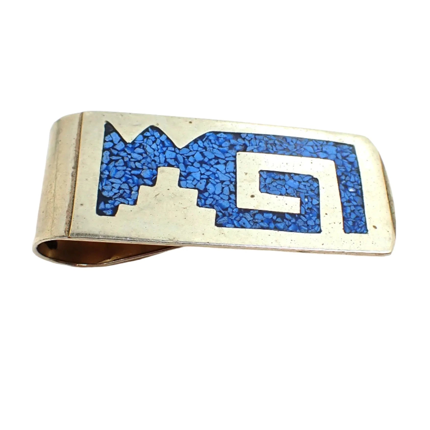 Angled view of the 1980's vintage money clip. It is silver tone in color with blue dyed faux turquoise stone chips inlaid in a Mexican Southwestern style design.