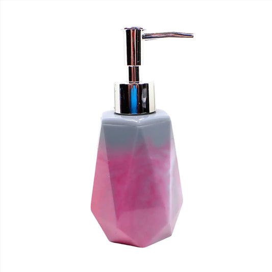 Side view of the handmade soap dispenser. It is faceted with a tapered top and flared bottom. The resin is marbled with shades of pink and gray. The pump in the photo is silver in color.