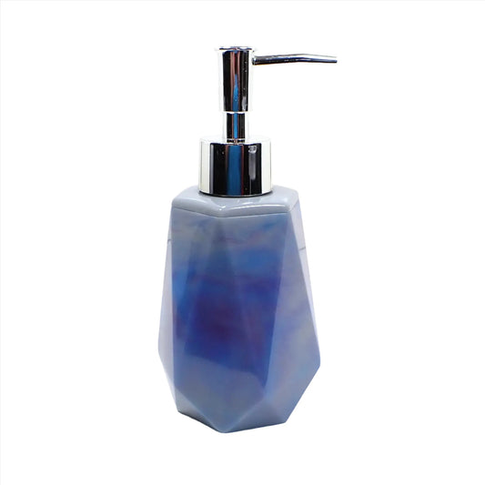 Side view of the marbled multi color handmade resin soap dispenser. It is faceted shaped with a tapered top and flared bottom. It has marbled shades of blue, purple, and gray color. The pump on top in the photo is silver in color.