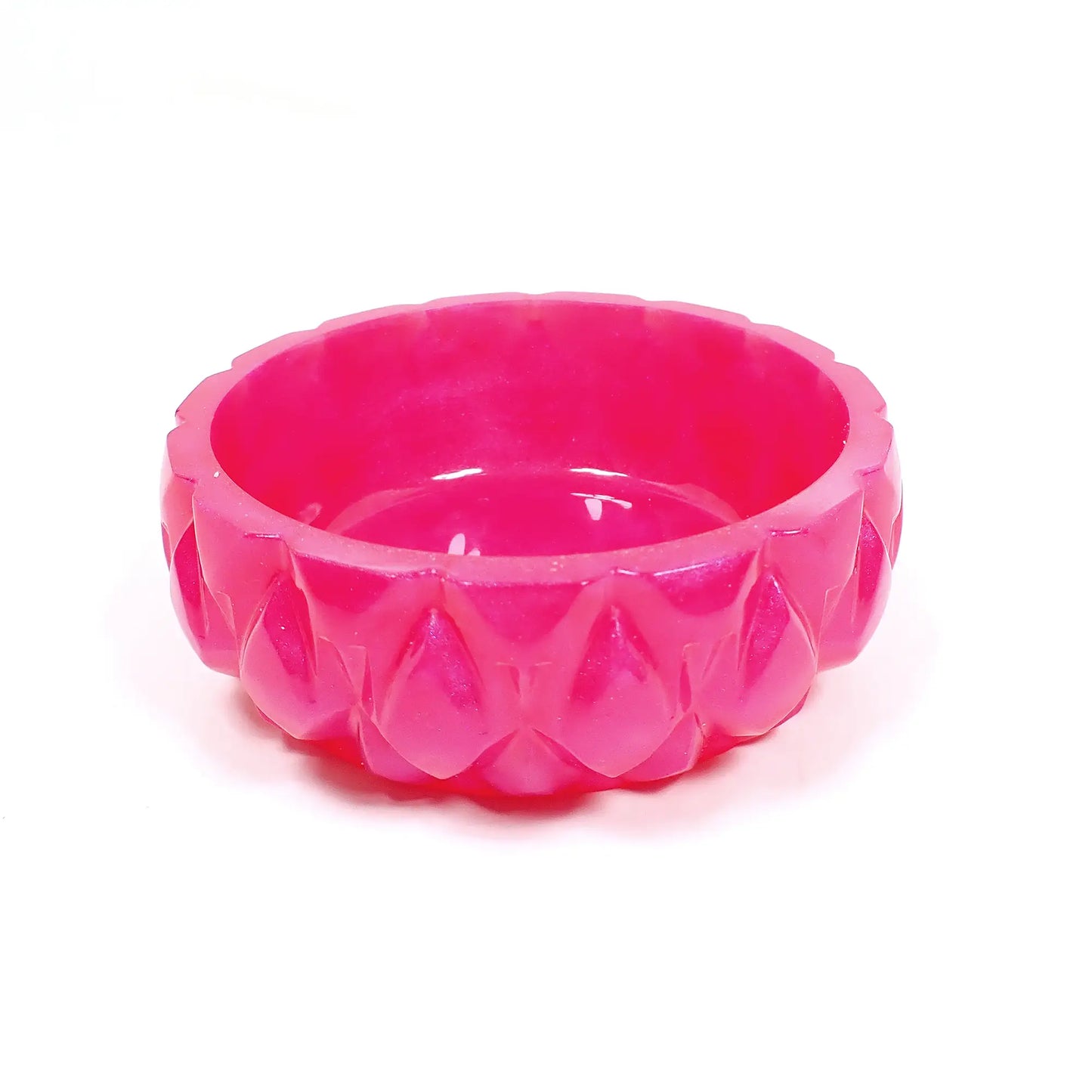 Angled view of the small handmade decorative bowl. It is bright pearly pink in color with a faceted geometric design around the outside edge.