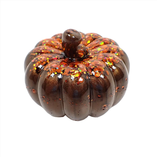 Side view of the small handmade resin pumpkin. It is pearly dark brown in color with chunky iridescent orange glitter on top.