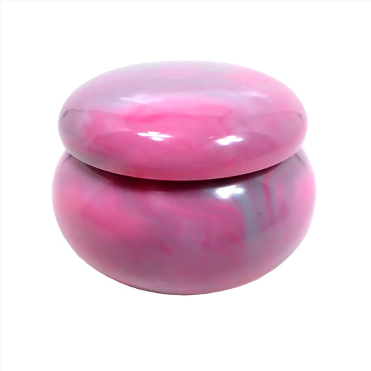 Side view of the small handmade resin decorative jar trinket box. The resin is marbled in shades of pink and gray. It is round shaped with a rounded lid.
