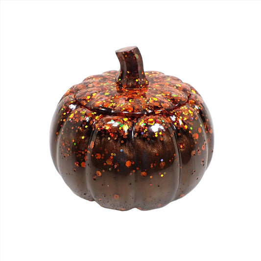 Side view of the handmade resin pumpkin trinket box. This decorative jar has pearly dark brown resin with chunky iridescent orange glitter on top.