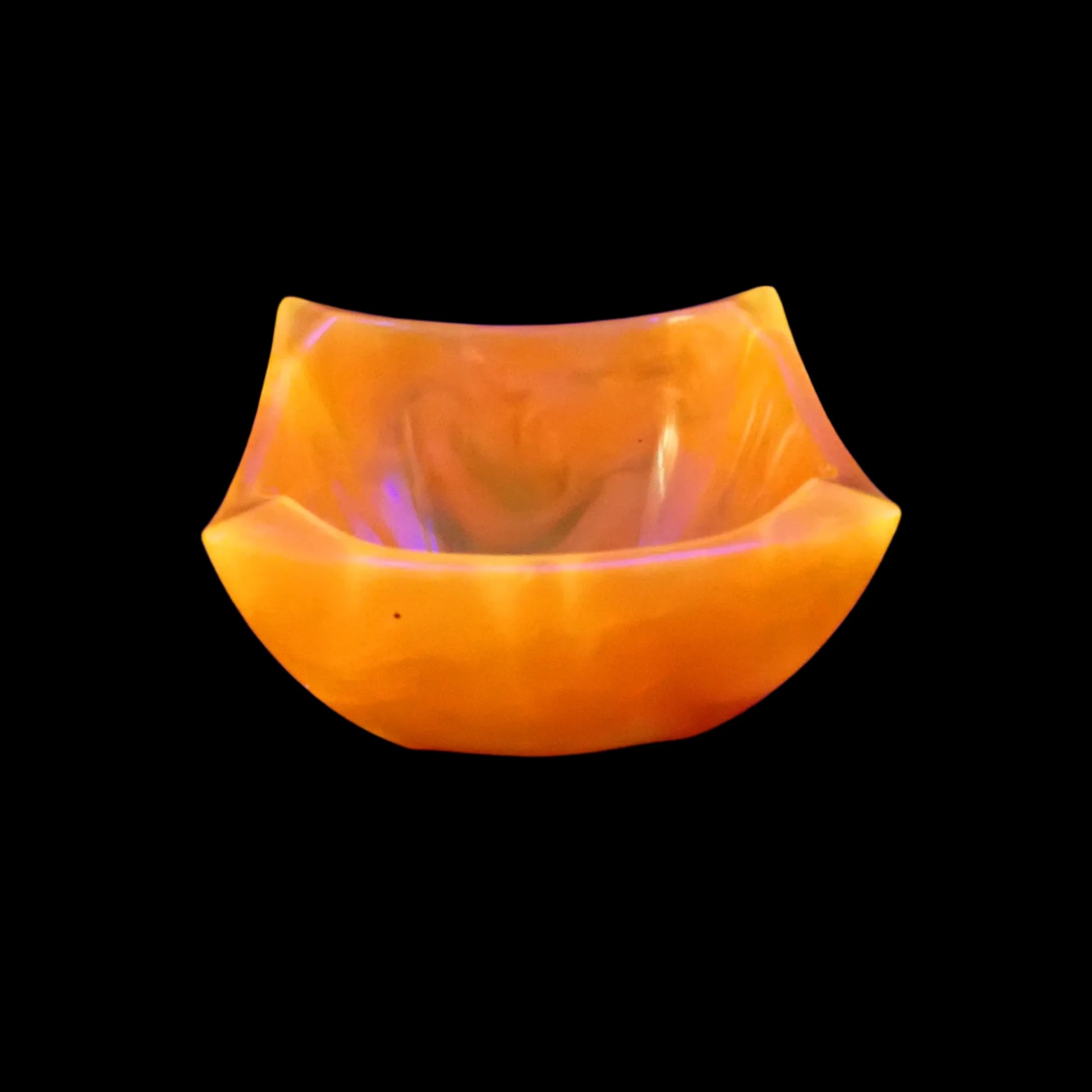 Photo of the handmade neon orange 
resin angled bowl showing how it fluoresces orange under a UV light.