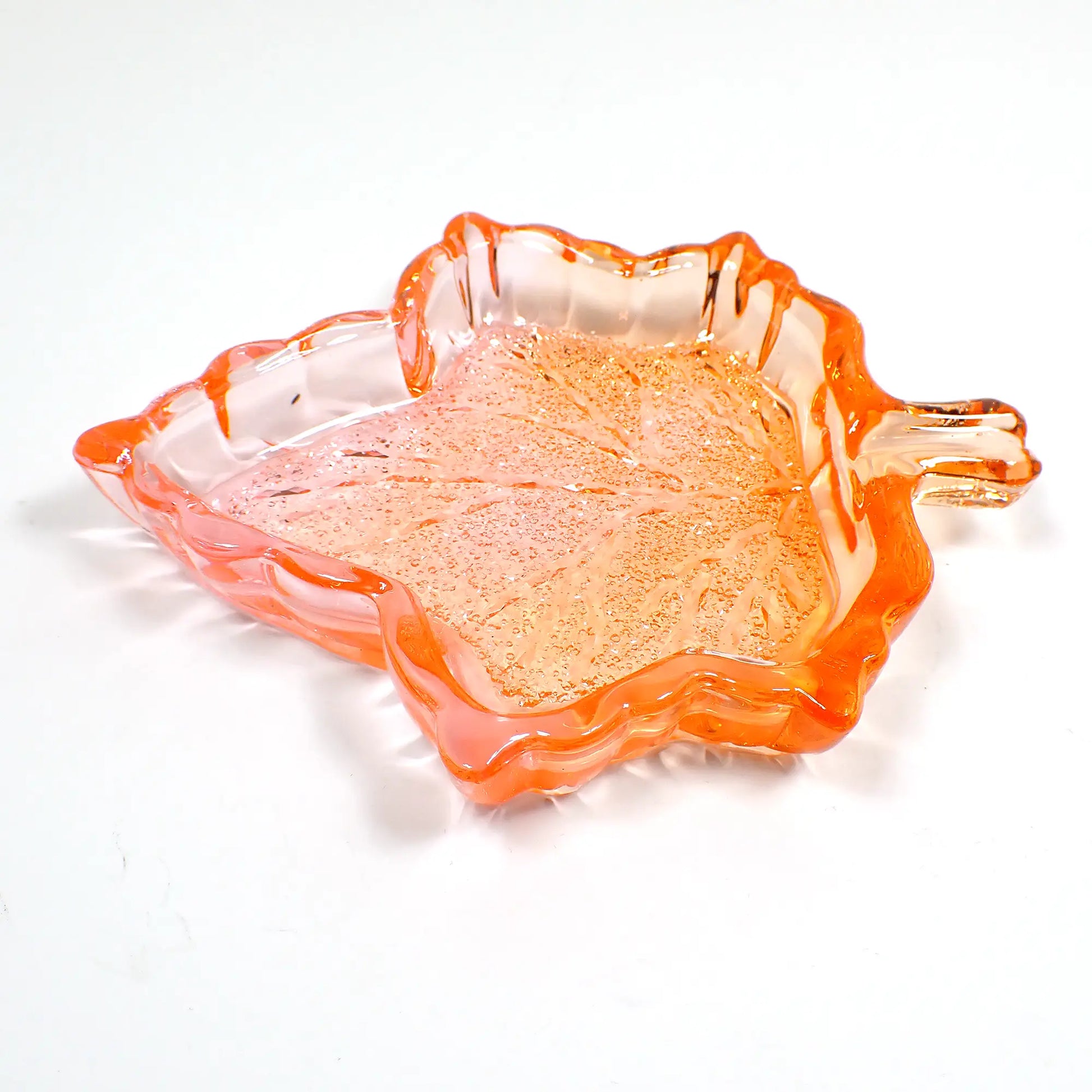 Angled view of the handmade Fall leaf decorative trinket dish. It's shaped like a maple leaf and has translucent orange resin with hints of pink. The inside bottom has a crystal like design that sparkles as the light as hitting it. 