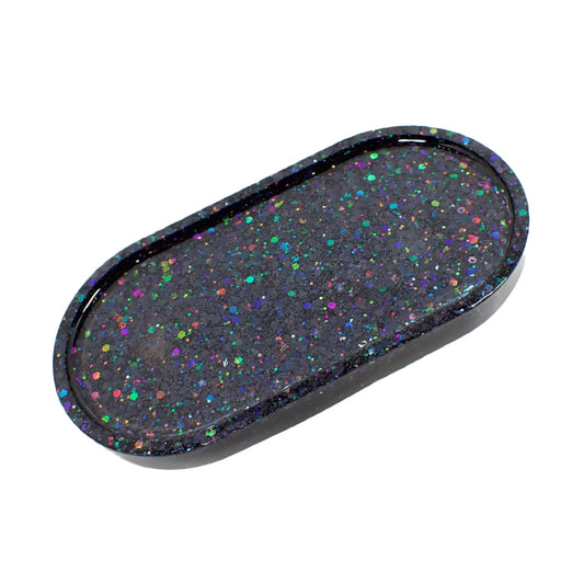 Angled view of the Goth handmade oval resin trinket dish. It has black resin with rainbow color chunky iridescent glitter.