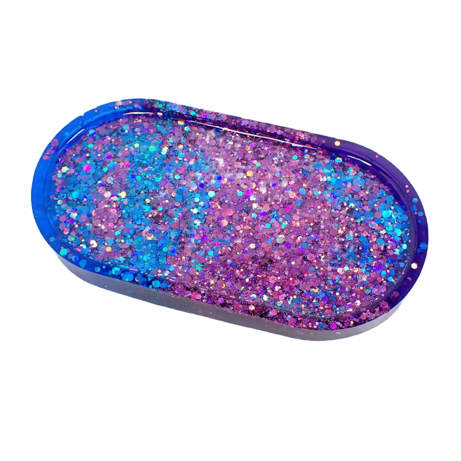 Angled view of the handmade resin oval trinket dish. It has pearly blue resin on one side and pearly purple resin on the other. There is iridescent blue and purple glitter on top.