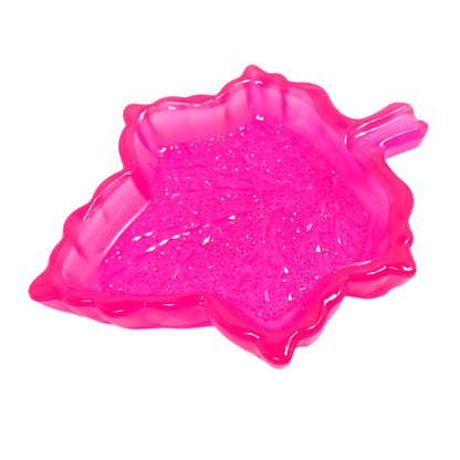 Angled view of the handmade resin leaf trinket dish. The resin is bright neon pink in color. The inside bottom of the leaf has a faceted crystal like design that sparkles in the light.