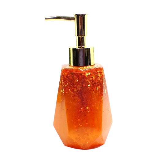 Side view of the handmade resin soap dispenser. This photo shows it with a gold color pump on top. The bottle part has pearly bright orange resin on the bottom and chunky iridescent orange  glitter on top. It has a faceted shape with a flared out bottom.