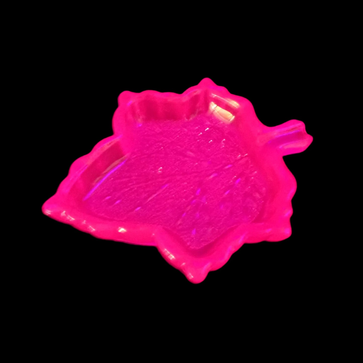 Photo showing how the handmade neon pink resin leaf trinket dish fluoresces bright pink under a UV light.