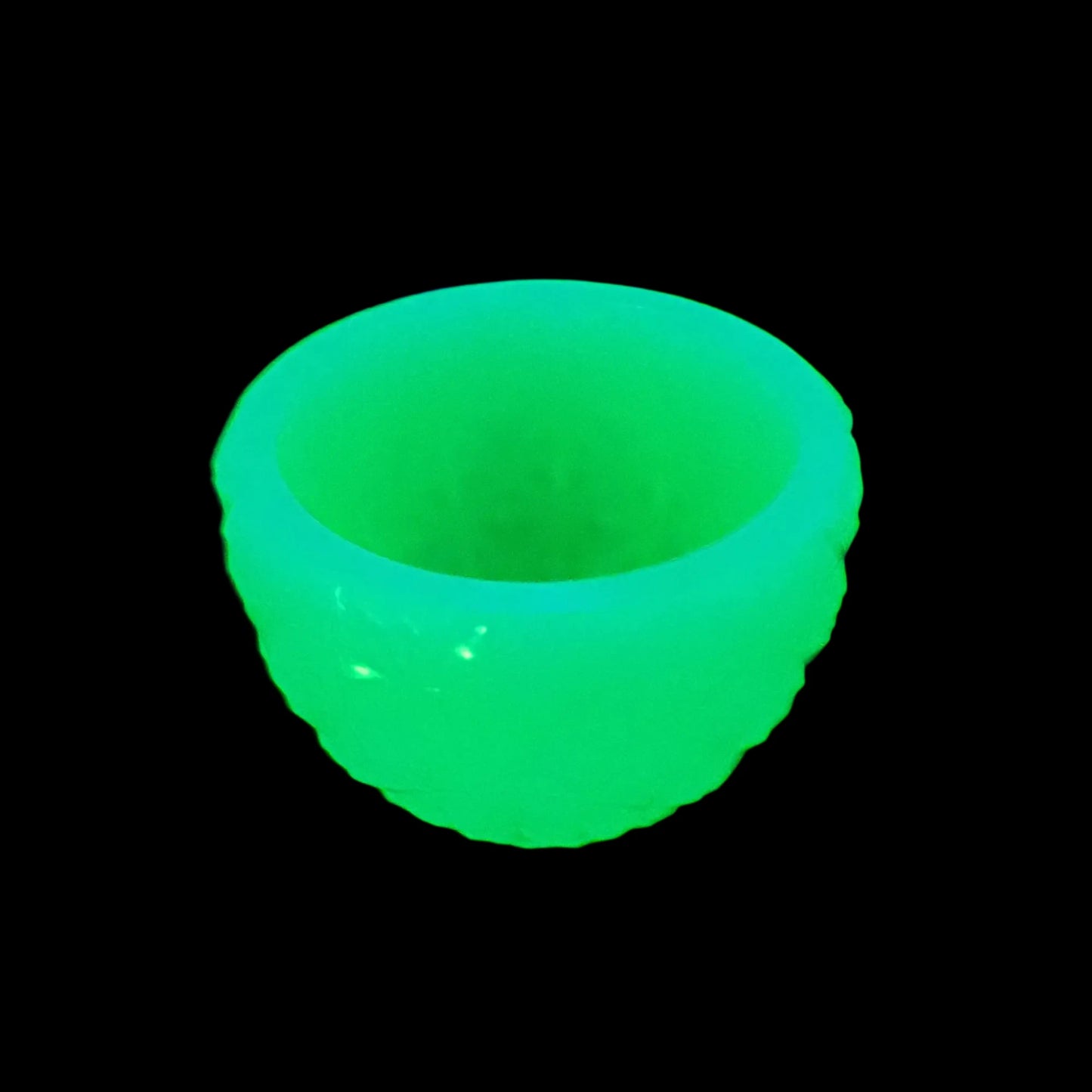 Photo of the handmade neon green resin retro style faceted decorative bowl showing how it fluoresces bright green under a UV light.