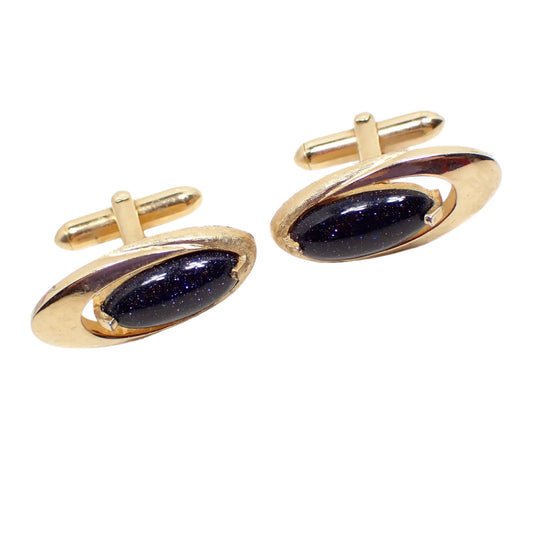 Front view of the Swank Mid Century vintage cufflinks. They have an Atomic Style oval design with domed oval blue goldstone glass cabs. The metal is gold tone in color.