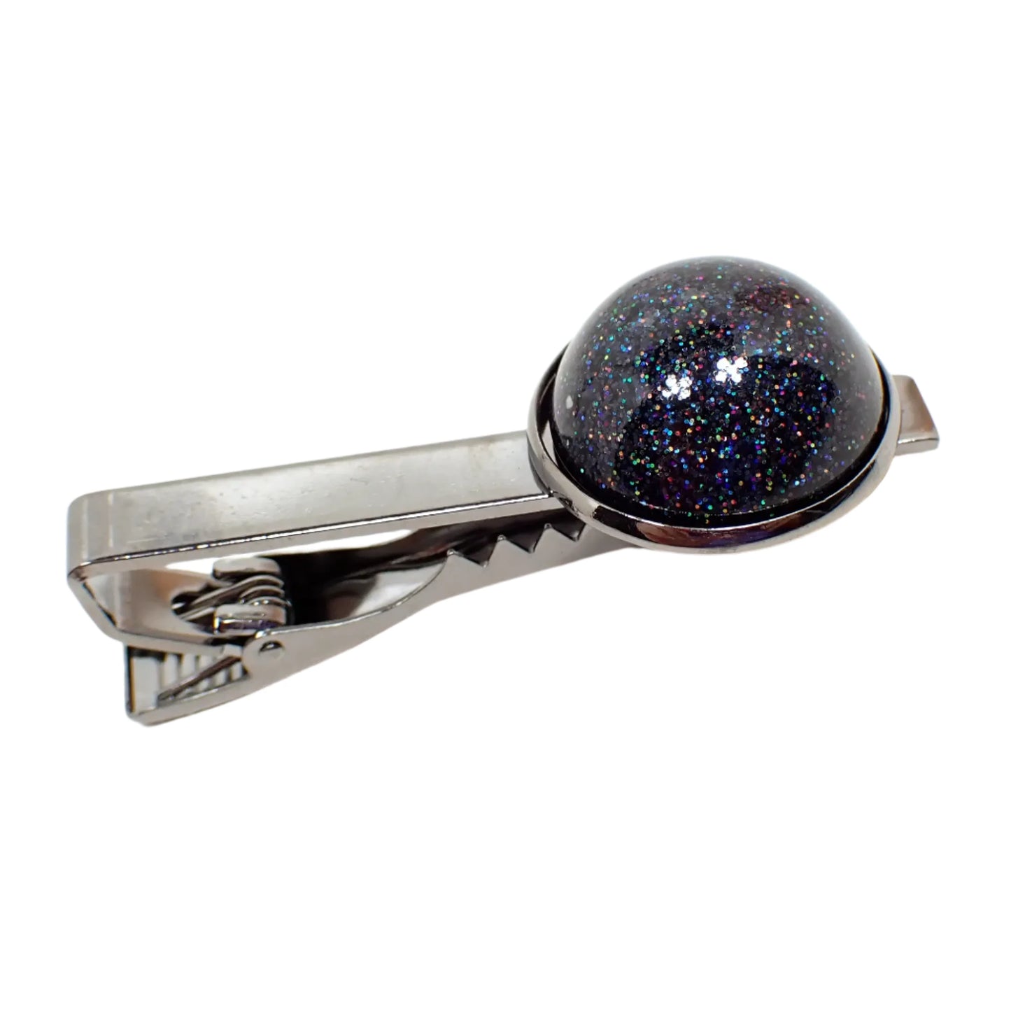 Angled view of the black holographic tie clip. The metal is gunmetal gray in color. There is a domed round handmade resin cab at the end that has black holographic glitter that has tiny sparkles of different colors as the light hits it.