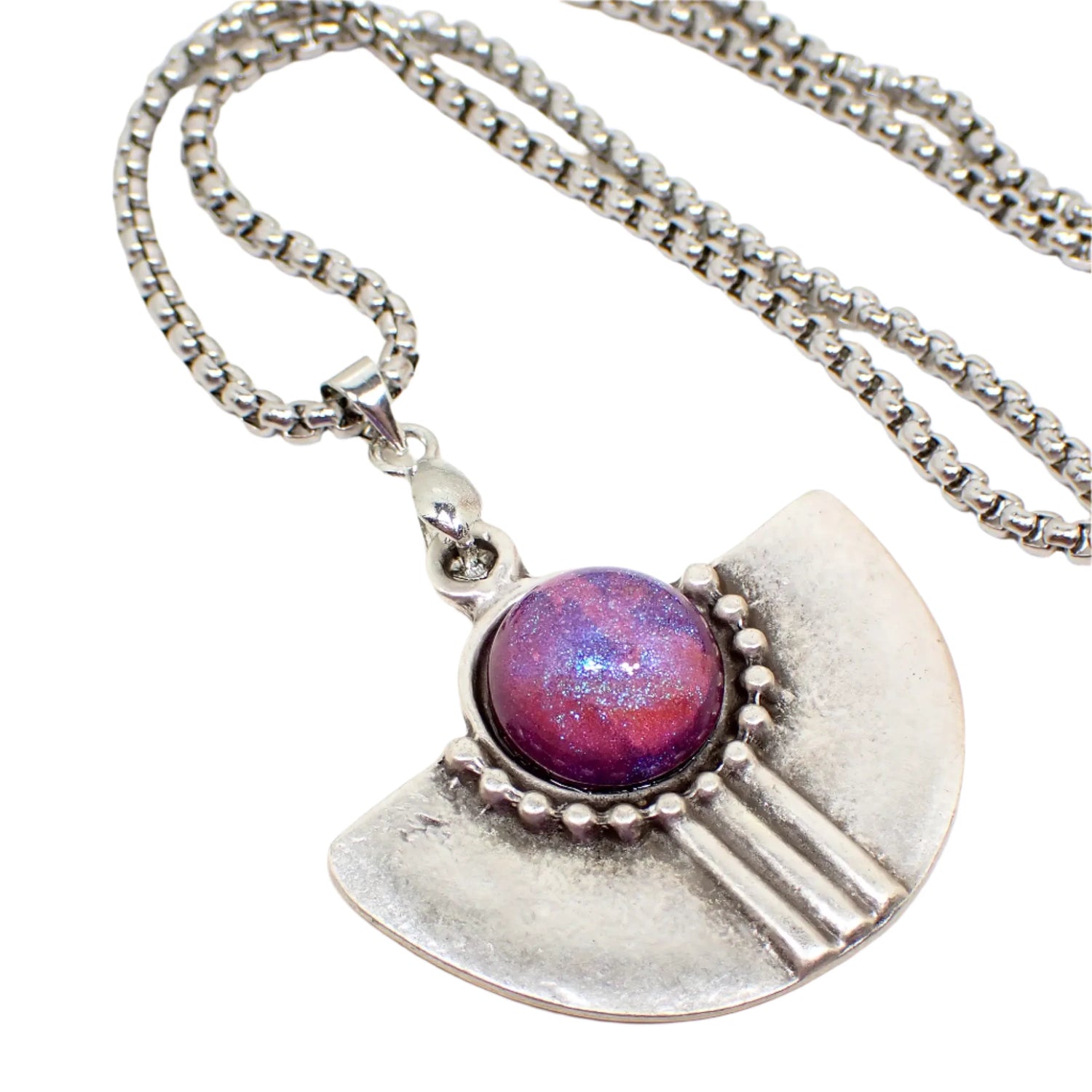 Enlarged view of the Boho style pendant necklace. The pendant has a semi circle shape with a domed round handmade resin cab at the top. The cab has a color shift design that goes from pink to purple and blue depending on how the light hits it. The metal is antiqued silver in color.