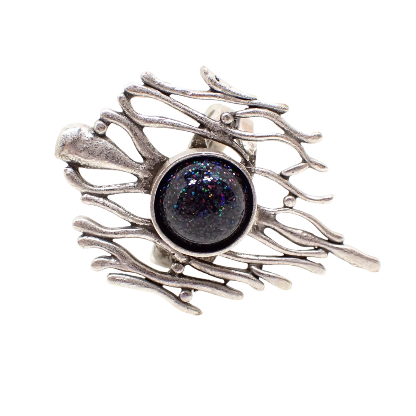 Angled view of the handmade brutalist style adjustable ring. The metal is silver tone in color and it has a small domed round cab in the middle that is black resin with holographic black glitter. The glitter sparkles tiny different specks of the colors of the rainbow as the light hits it.