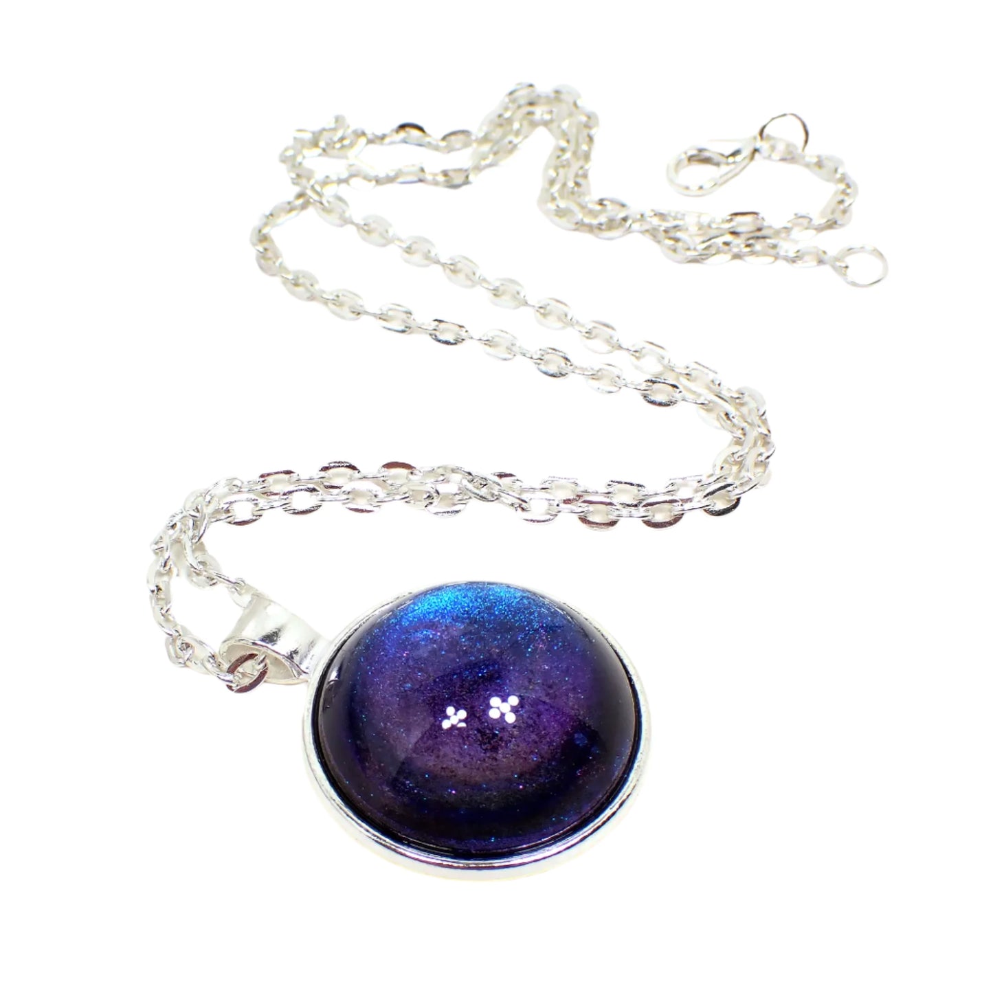 Angled view of the handmade color shift round resin pendant necklace. The metal is silver tone in color. The round pendant has a domed round cab with a color shift design that goes from blue to purple depending on how the light is hitting it.