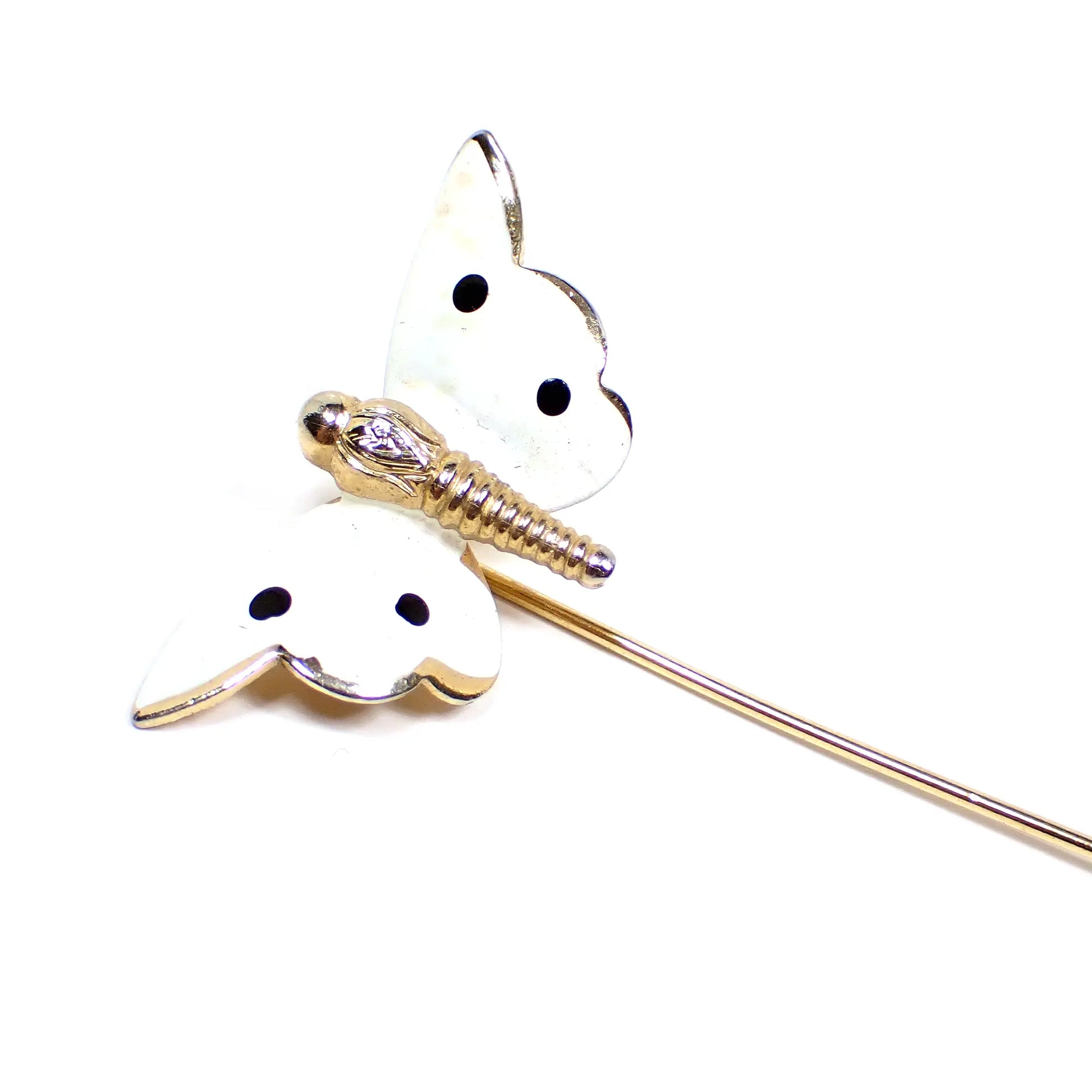 Enlarged view of the Mid Century vintage butterfly stick pin. The metal is gold tone in color. The wings of the butterfly are white enameled with 4 black enameled spots.