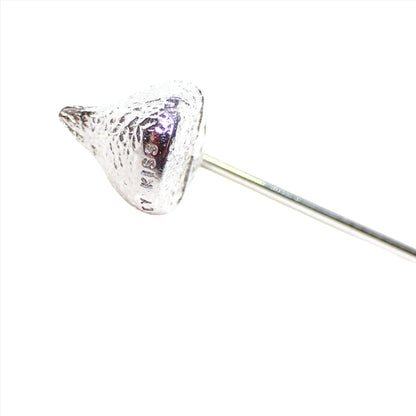 Enlarged view of the Hershey's retro vintage stick pin. The metal is silver tone in color. The top is shaped like a Hershey's kiss. The word Kiss can be see stamped on the bottom area.