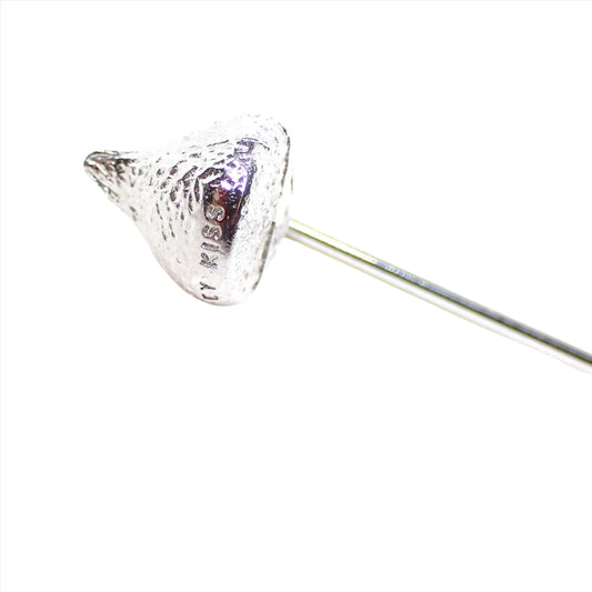 Enlarged view of the Hershey's retro vintage stick pin. The metal is silver tone in color. The top is shaped like a Hershey's kiss. The word Kiss can be see stamped on the bottom area.