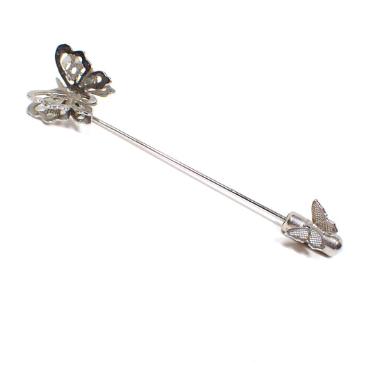 Full view of the Mid Century vintage butterflies stick pin. The metal is silver tone in color. The top has a butterfly with a cut out double wing style design. The clutch on the bottom of the pin has a smaller sized textured butterfly on it.