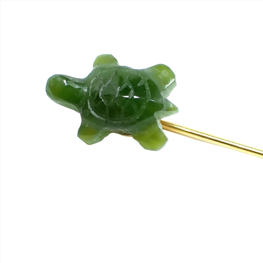 Enlarged view of the Mid Century vintage carved jade stick pin. The metal is gold tone in color. The top has a carved jade turtle that is a lovely shade of green.