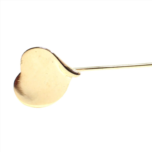Enlarged view of the retro vintage curvy heart stick pin. The metal is gold tone in color. There is a heart shape at the top that is curved slightly at the edges.