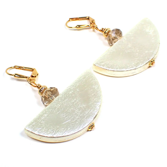 Angled view of the handmade half moon earrings. The metal is gold plated in color. There is a faceted glass crystal bead at the top with shades of light brown and clear. The bottom beads are vintage acrylic beads that are half moon shaped with a textured design in a golden off white color.