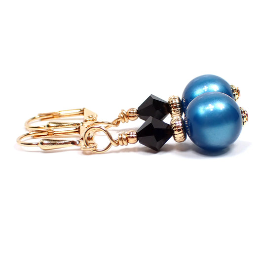 Side view of the handmade small drop earrings made with vintage moonglow lucite beads. The metal is gold plated in color. There is a black faceted glass crystal bead at the top. The bottom moonglow lucite bead is round ball shaped and is teal blue in color.