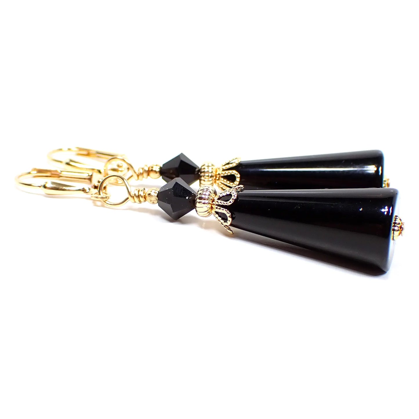 Side view of the handmade cone earrings with vintage lucite beads. The metal is gold plated in color. There is a faceted bicone glass crystal bead at the top in black. The bottom lucite bead is cone shaped with the tapered end at the top and it is also black in color.