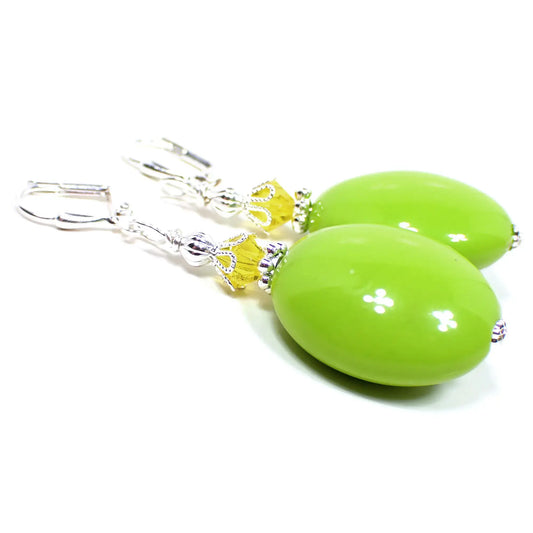Side view of the handmade large oval drop earrings. The metal is bright silver in color. There is yellow faceted glass crystal bead at the top. The bottom bead is a large acrylic oval shape in lime green color.