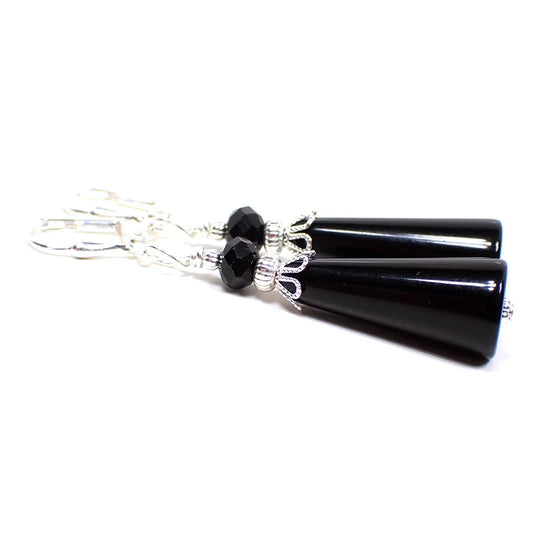 Side view of the handmade lucite cone earrings. The metal is bright silver in color. There is a faceted glass black bead at the top. The bottom bead is cone shaped with the tapered end at the top. It is a vintage black lucite bead.