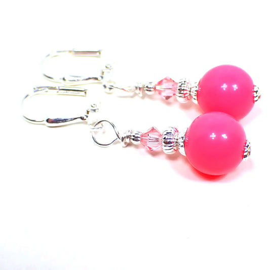 Top view of the handmade small drop earrings with vintage acrylic beads. The metal is bright silver in color. There is a faceted glass crystal bead in light pink at the top. The bottom acrylic beads are round ball shaped and are bright pink in color.