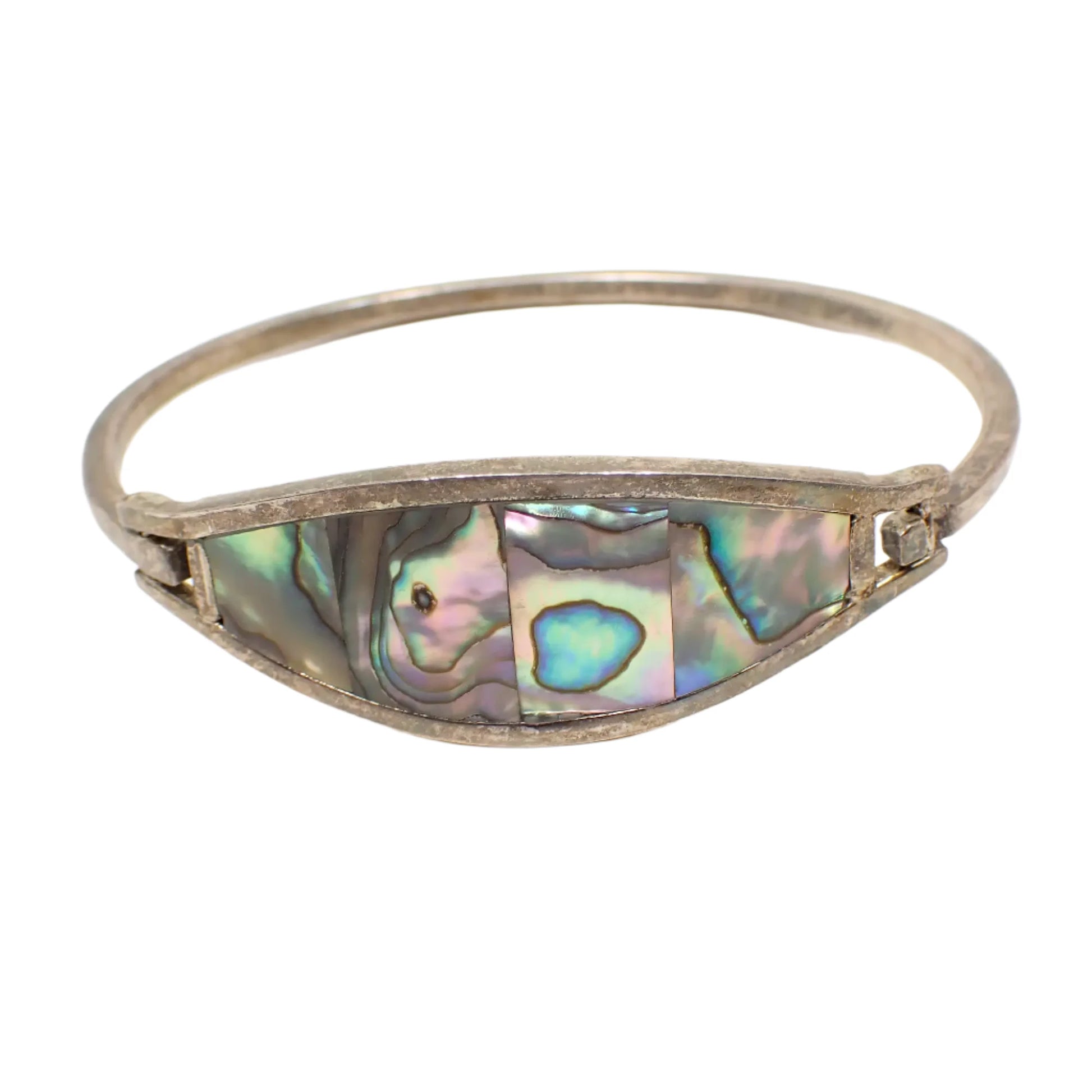 Front view of the vintage Alpaca hinged bangle bracelet. The metal is antiqued silver tone in color. There is an area on the front of the bracelet with four large pieces of inlaid abalone shell. The shell pieces have different pearly colors showing.