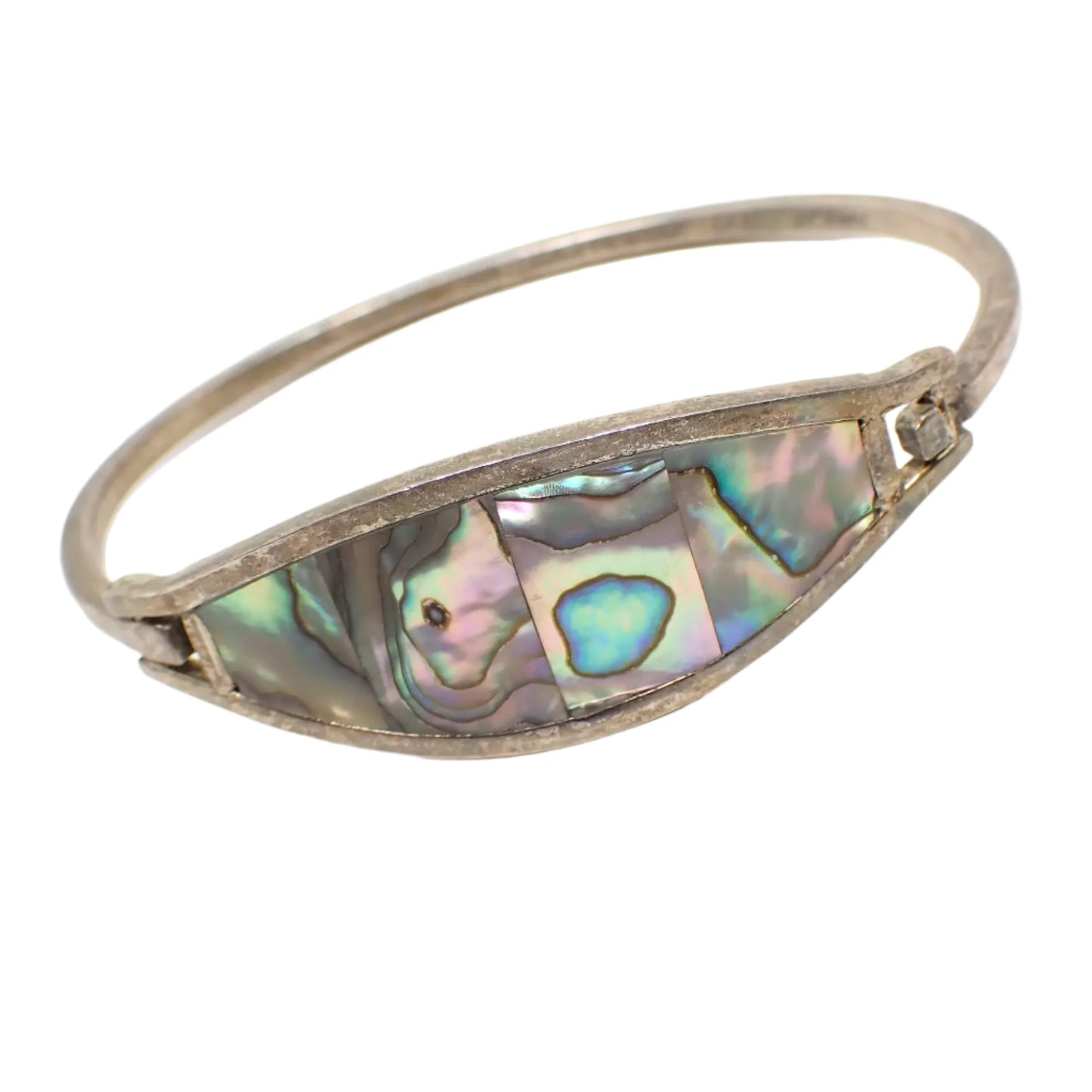 Angled view of the vintage Alpaca abalone hinged bangle bracelet. More of the inside area of the bracelet can be seen in the photo. It has an antiqued silver tone appearance.