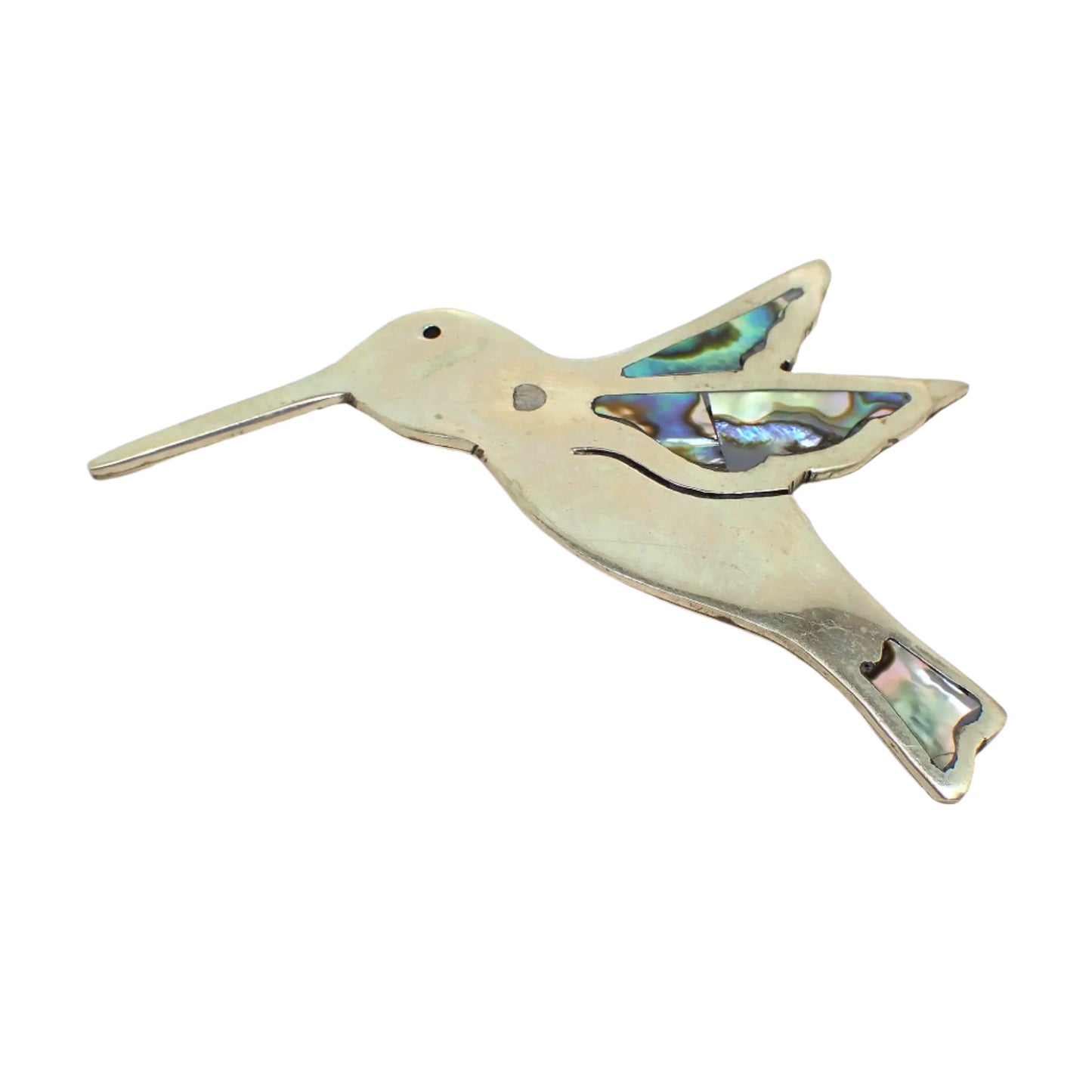 Front view of the retro vintage alpaca hummingbird brooch. The metal is silver tone in color and is shaped in a flat hummingbird design. There is a small black dot for the eye and inlaid abalone shell on the wings and tail area. A darker color spot can be seen on the birds neck.