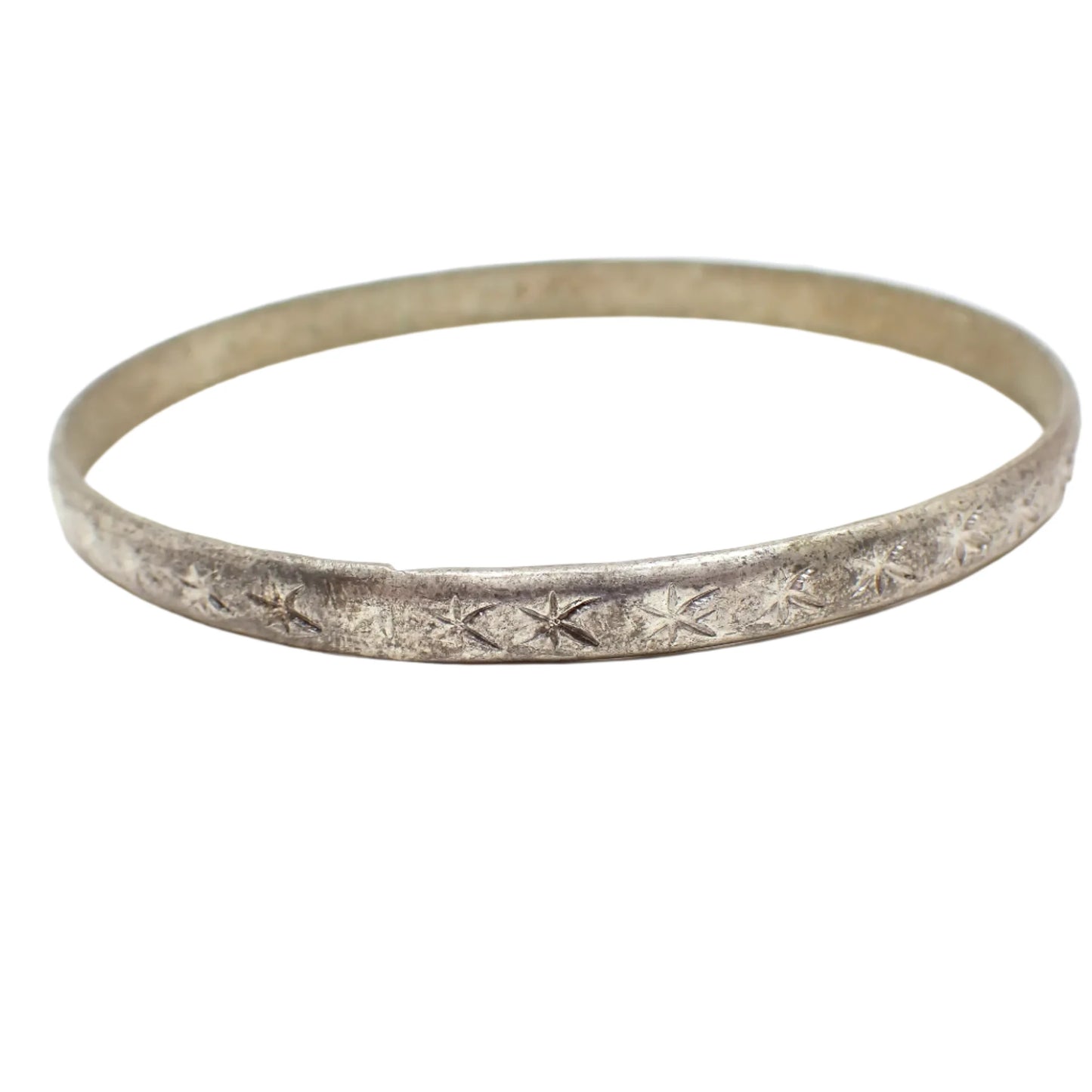 Angled side view of the Mid Century vintage bangle bracelet. It has a stamped atomic star design around the outside and is antiqued silver in color.