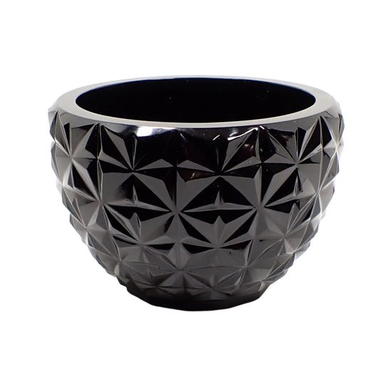 Angled side view of the retro style handmade resin decorative bowl. It is shiny black in color and is round with a tapered bottom. There is a faceted design all the way around the outside.