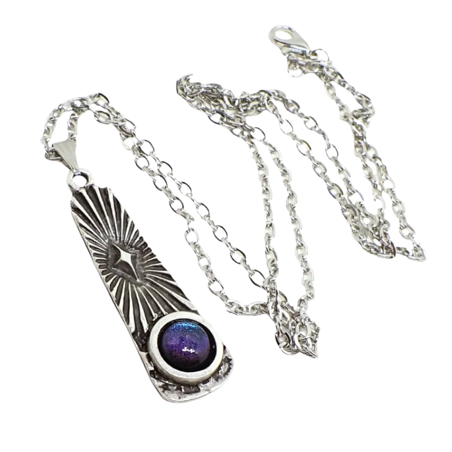 Photo of the entire pendant necklace. The metal is antiqued silver in color. There is a cable chain with lobster claw clasp and a long oval like shaped pendant with flared bottom. The top part of the pendant has an atomic star and rays of light design and the bottom has a domed round cab with color shift resin that goes from blue to purple depending on how the light hits it.