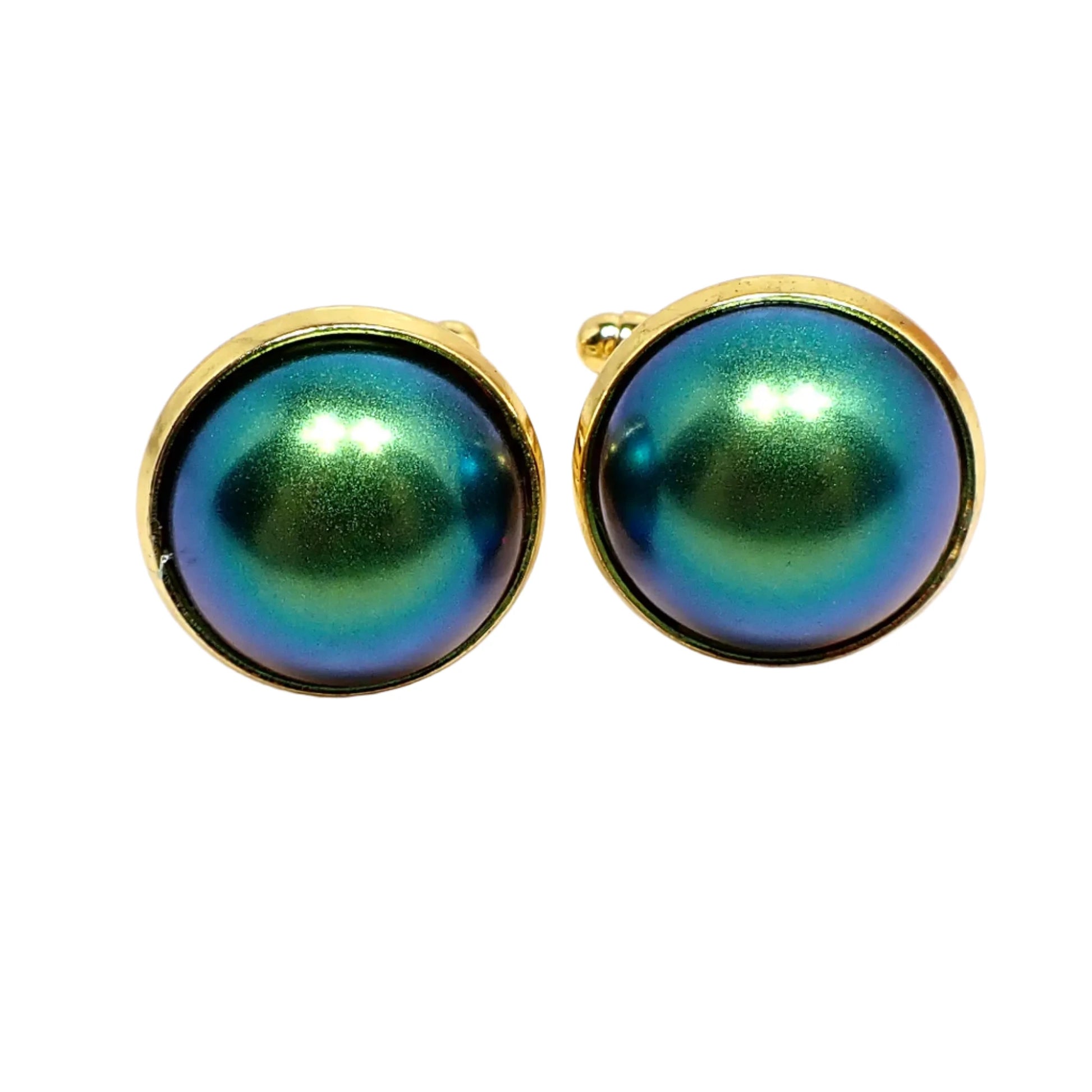 Front view of the color shift cufflinks. The metal is gold tone in color. They are round with domed round resin cabs. The cabs are matte metallic that mostly have shades of blue and green with hints of purple around the edge.