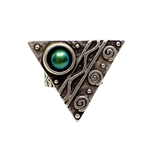 Front view of the geometric triangle ring. The metal is antiqued silver in color. One side has raised swirl shapes, the middle has lines with a curvy line in between, and the corner has a domed round resin cab with color shift resin that goes between blue and green depending on how the light is hitting it.