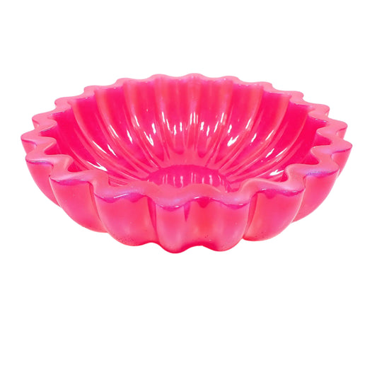Angled view of the handmade pearly bright pink resin decorative bowl. It has a round shape with tapered bottom, flat scalloped top edge, and fluted sides. The resin is opaque and pearly iridescent in a bright pink color with highlights of purple where the light is hitting it. Great as a succulent planter pot, part of your table centerpiece display, or just added to your home decor.