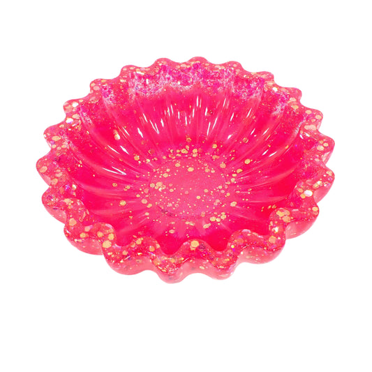 Angled view of the handmade resin scalloped bowl. The resin is a bright pearly pink in color with chunky iridescent glitter towards the top and bottom of the bowl. 