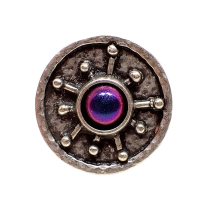 Front view of the starburst ring. It is antiqued silver in color and has a round shape with a starburst style design in the middle. There is a domed color shift resin cab and in this photo pink, blue, and purple can be seen.