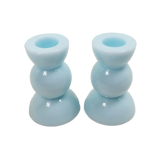 Angled view of the handmade resin candle holders. They are a light pastel cotton candy blue in color with a round geometric shape of a half sphere on top and bottom and a round sphere shape in the middle.