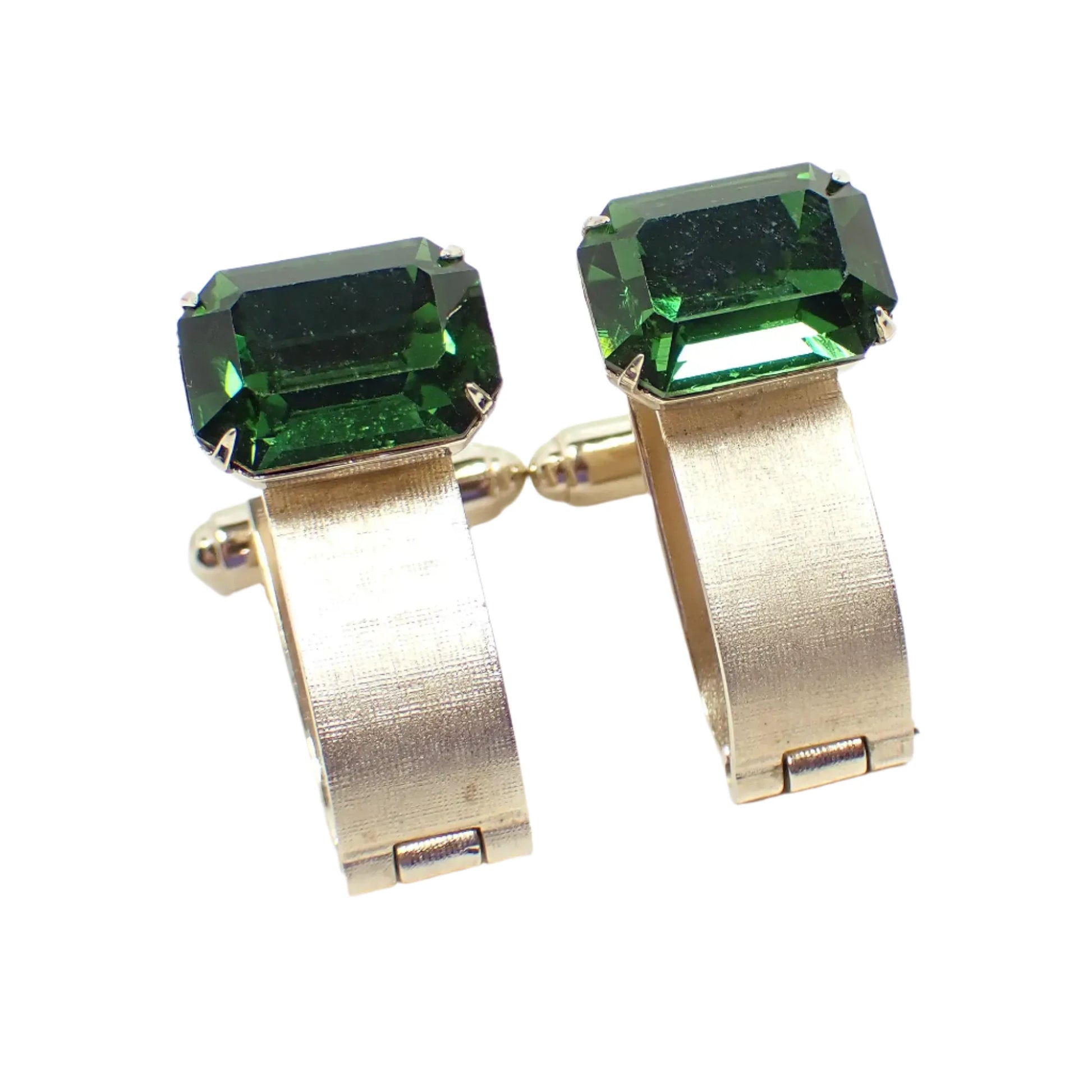 Angled front view of the Mid Century vintage Dante green rhinestone cufflinks. The metal is gold tone in color. There are emerald cut shaped rhinestones at the top in a forest green color. Curved matte metal bars come down from the rhinestones and wrap around to the back with a hinge at the bottom. 