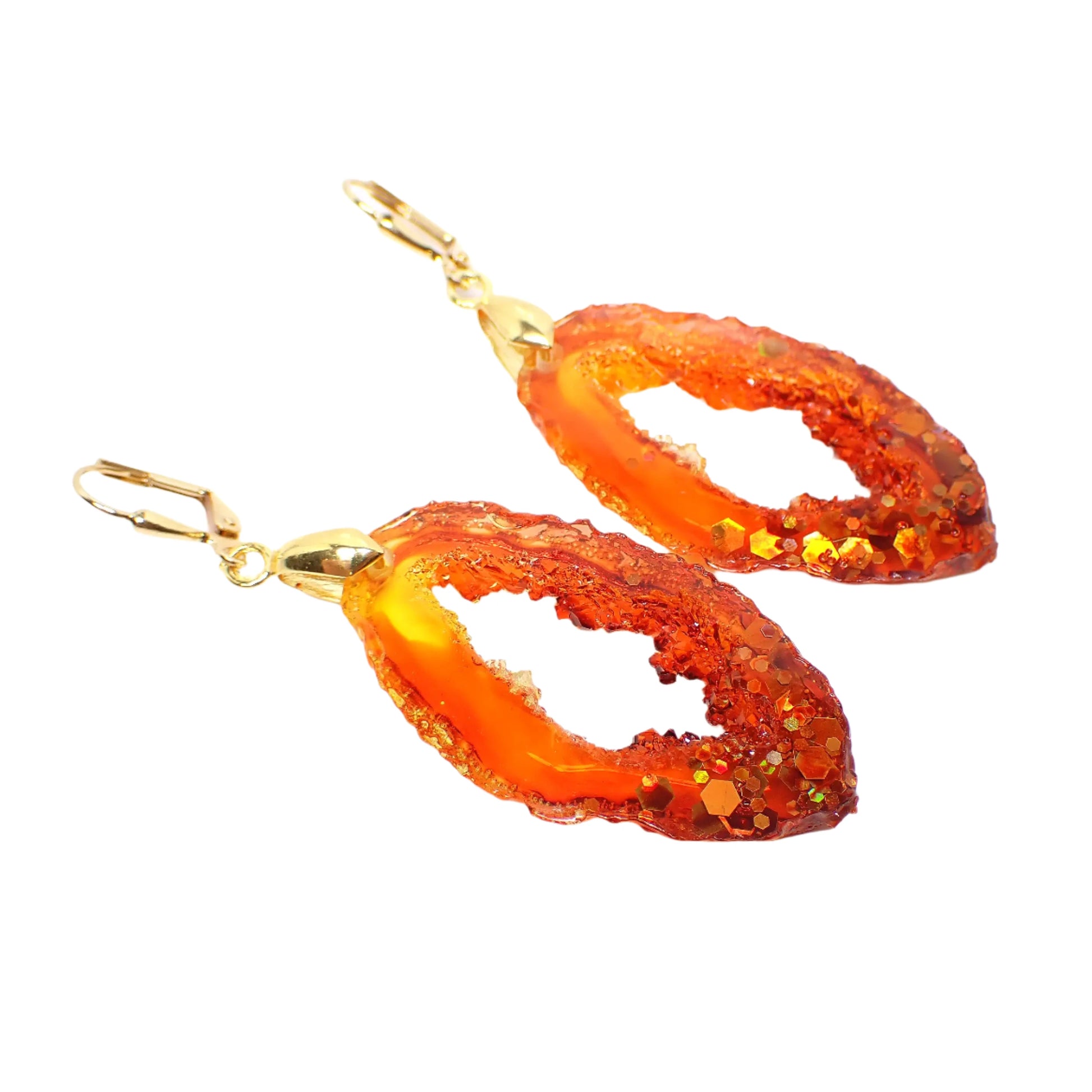 Angled front view of the handmade faux druzy geode slice style earrings. The metal is gold plated in color. The resin is mostly fiery red and orange with a hint of bright yellow at the top. There is chunky iridescent glitter at the bottom with shades of orange and yellow.