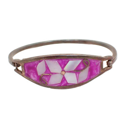 Front view of the vintage Alpaca hinged bangle bracelet. The metal has a darkened patina to a dark gray in color. The front has fuchsia colored enamel with inlaid pearly white pieces of mother of pearl shell forming a flower with leaves design.